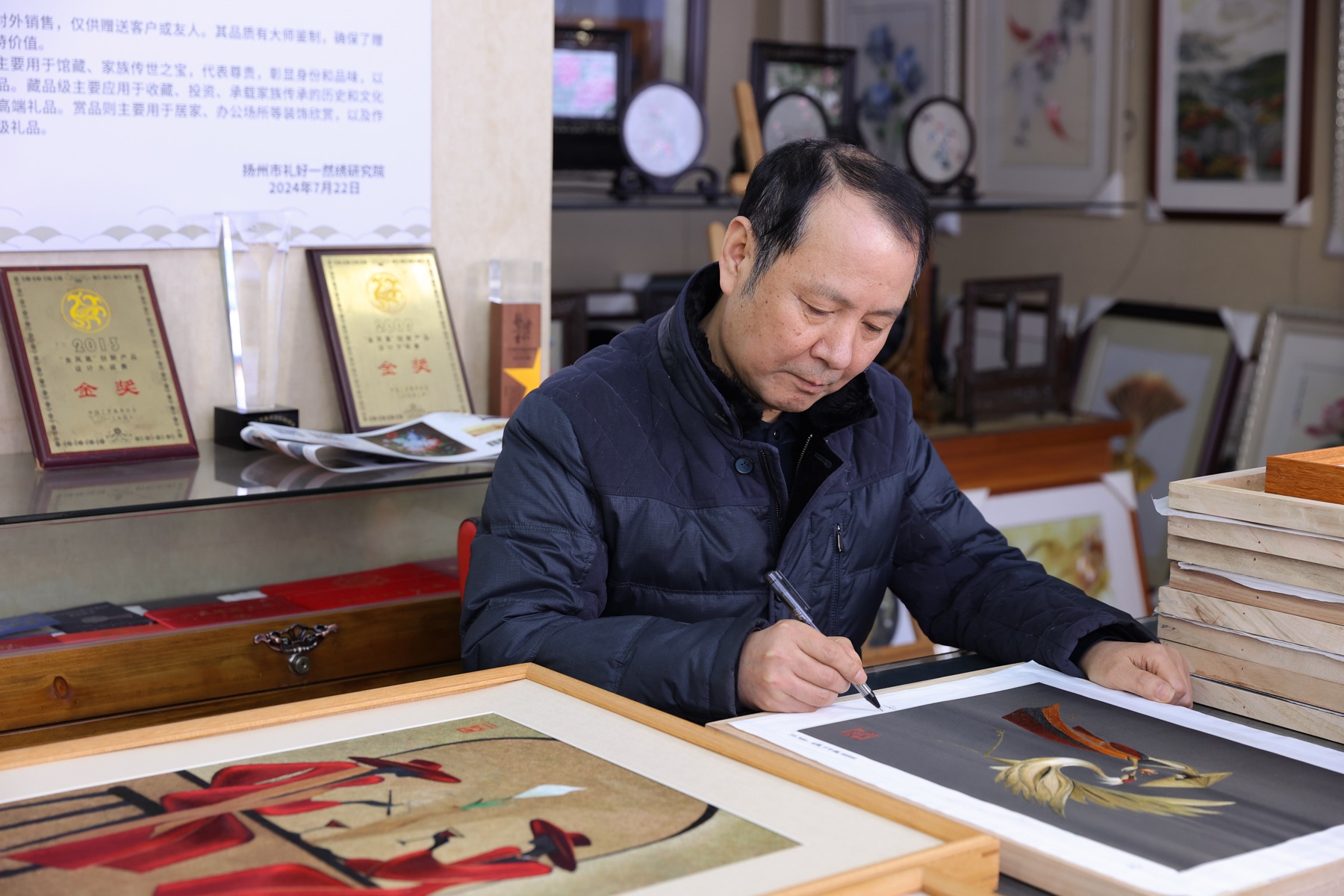 朱军成大师在工作室为完成的丝绣作品签名。